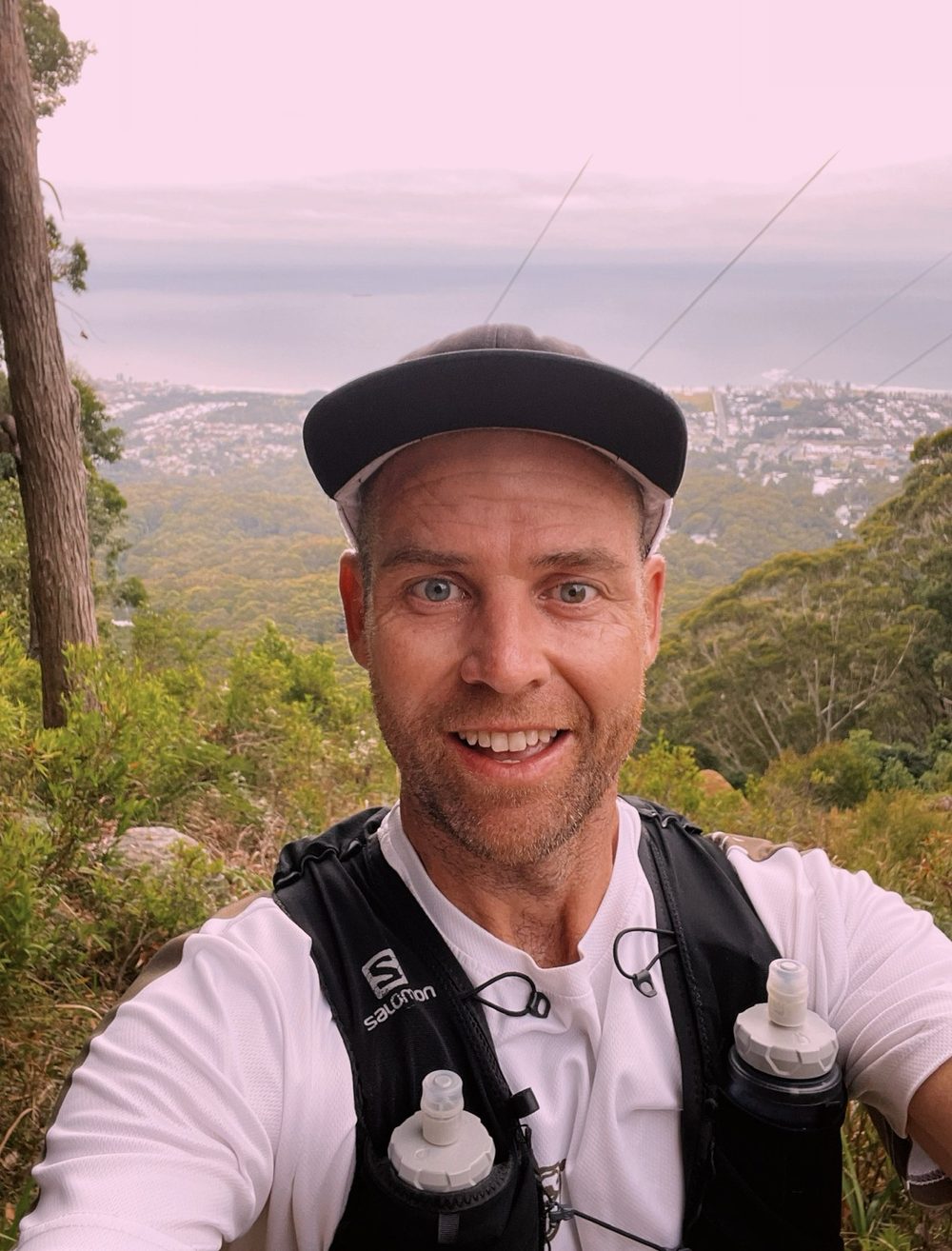 Johnnie Crawford on a trail run, with bushland and the coast behind him